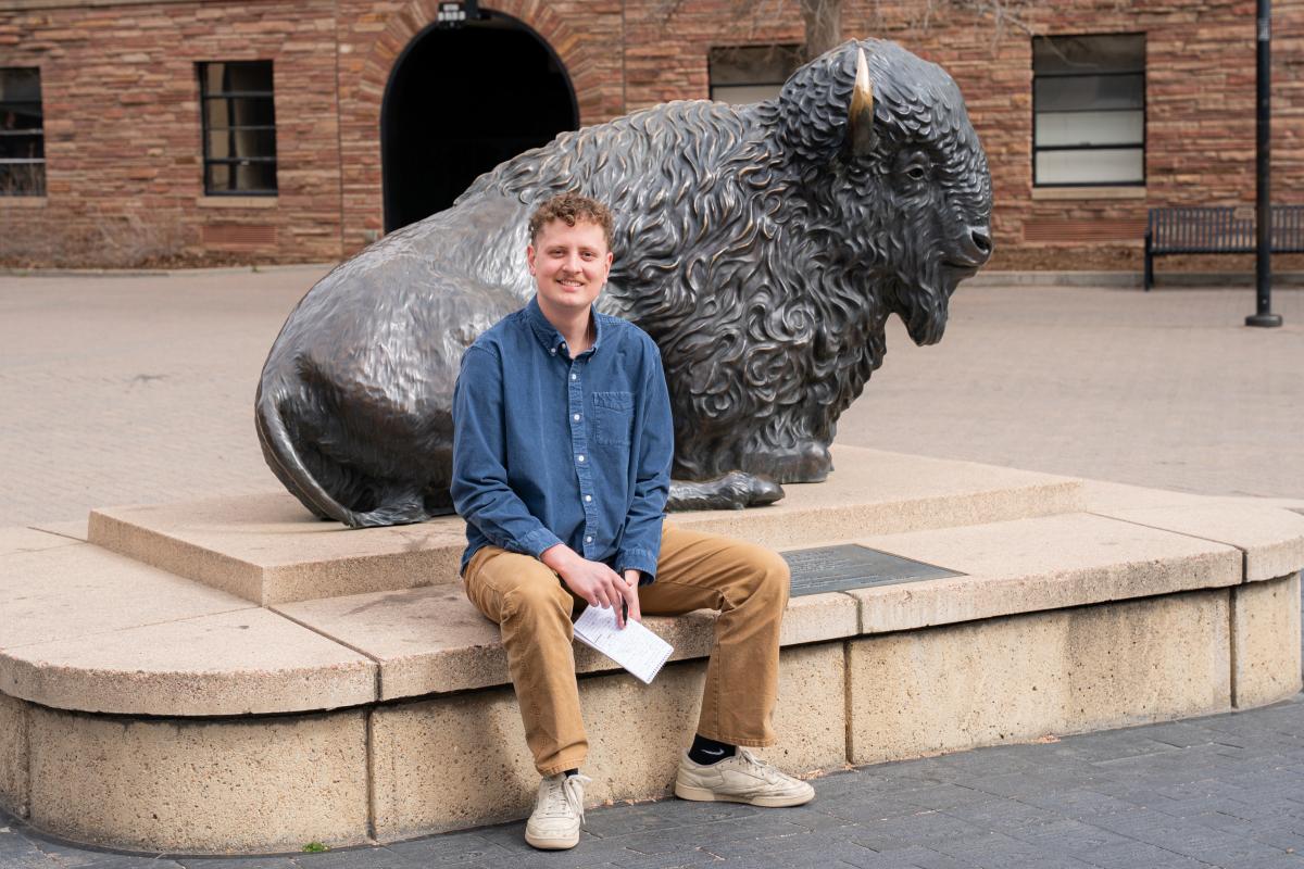 A student checks his notes in a reporter's notebook in front of a buffalo statue.