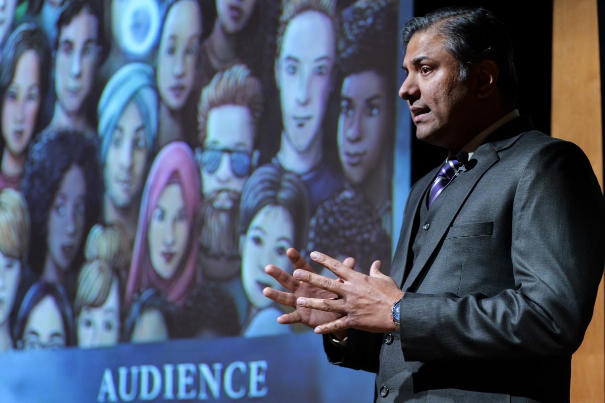A student in a suit presents in front of a slide.
