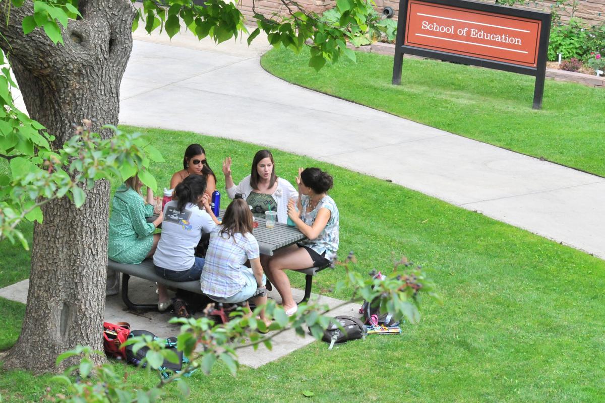 Students sitting at table outside the School of Education