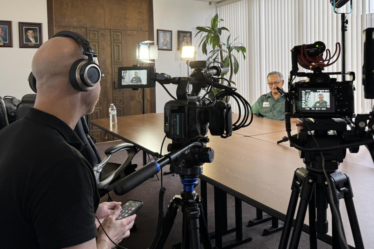 A professor prepares to interview a subject on camera in a conference room.